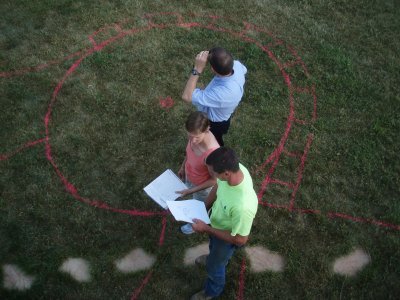 Three men making red outline in grass
