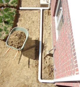 Trench with drainage pipe and wheelbarrow beside a brick building